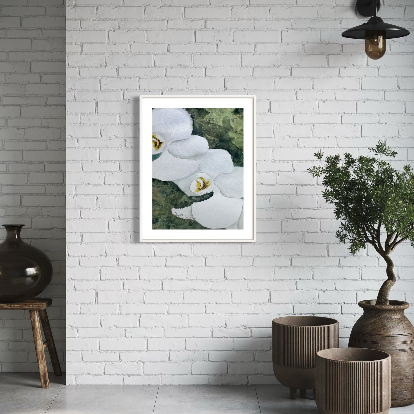 Framed artwork of white orchid flowers on a white brick wall with decorative vases and plants.