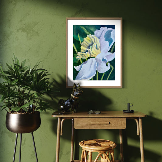 Framed yellow and white daffodil watercolor artwork on a green wall above a wooden desk with a plant and stool.