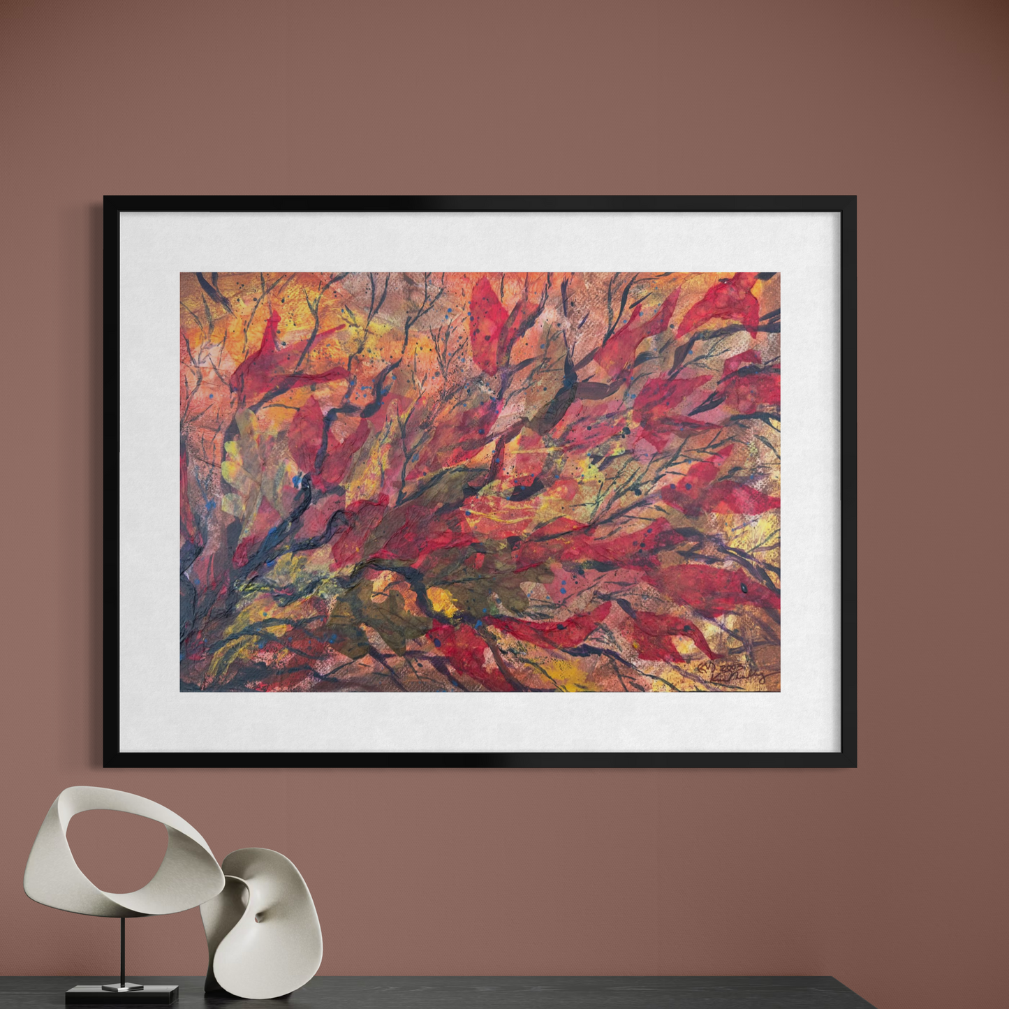 Framed abstract painting with vibrant colors on a brown wall above a table with a modern sculpture.