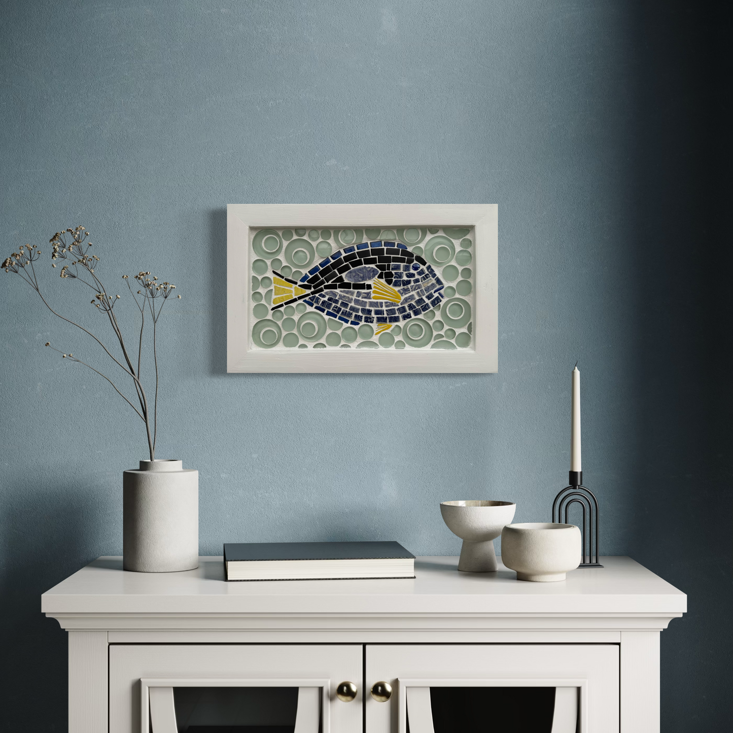 Decorative fish mosaic on a wall above a white cabinet with decorative items.