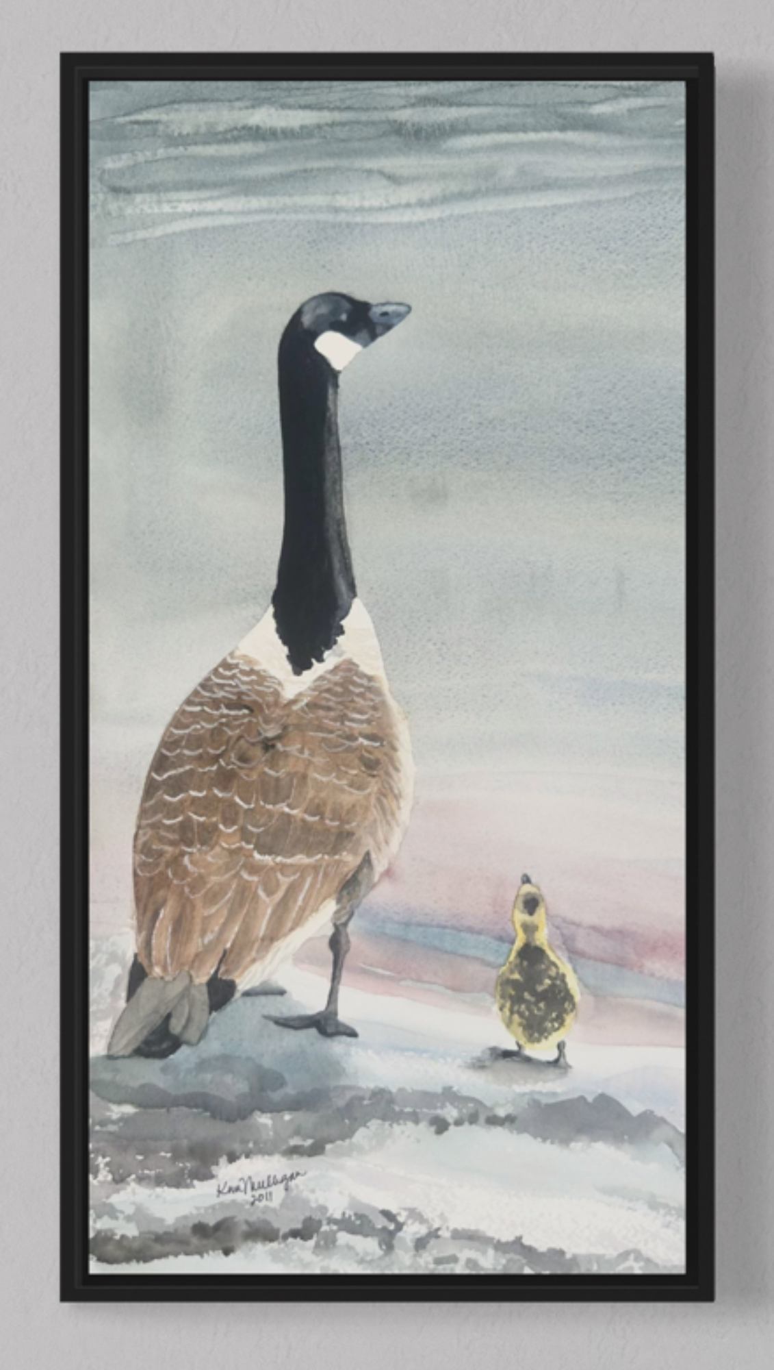 Framed artwork of a Canada goose and gosling looking out at the water from a beach.
