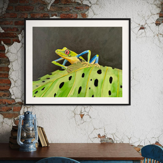 Framed watercolor artwork of a red eyed tree frog on a leaf against a textured wall.