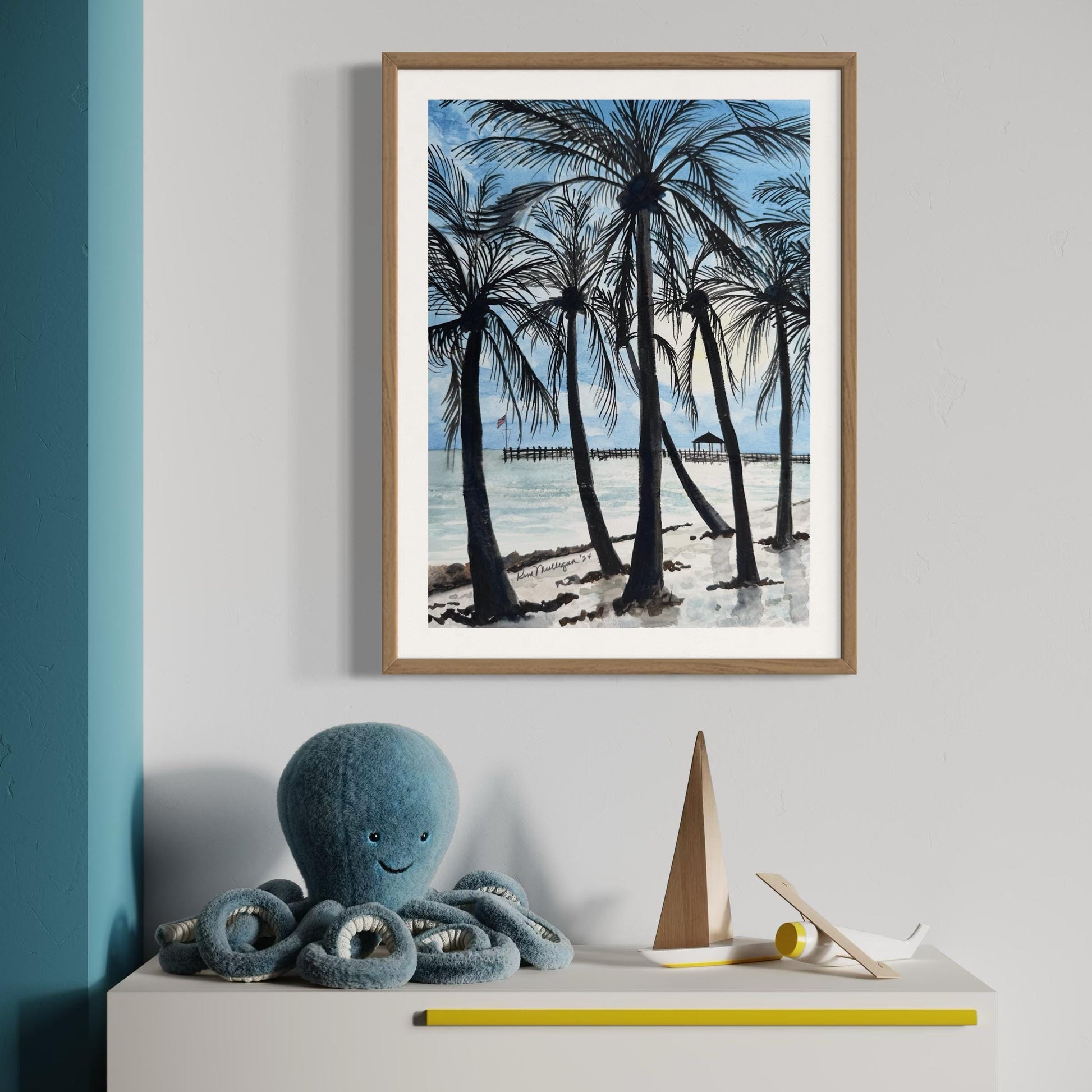 Framed watercolor painting of a beach scene with palm trees ocean and pier in the background.
