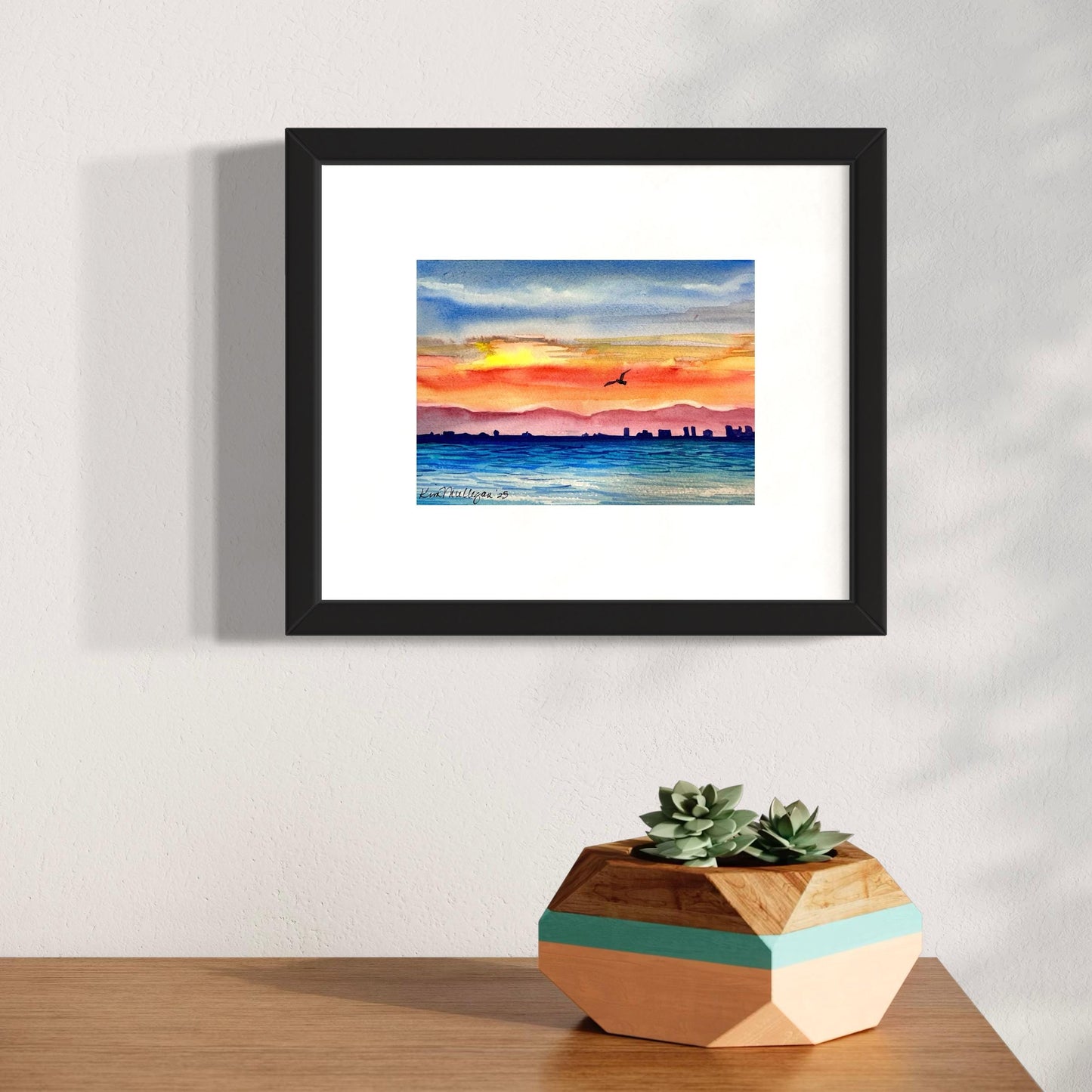 Framed watercolor art of sunset seen from a boat with city skyline in the background.