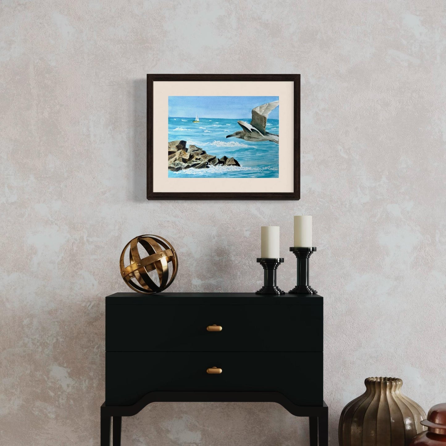 Framed watercolor artwork of a seagull flying over water with jetty rocks and a distant sailboat.