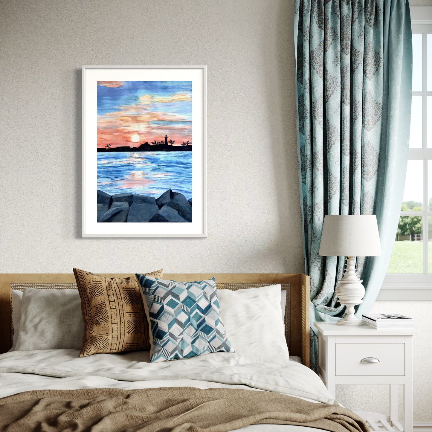 Framed artwork of a sunset over water on a wall above a bed with decorative pillows.