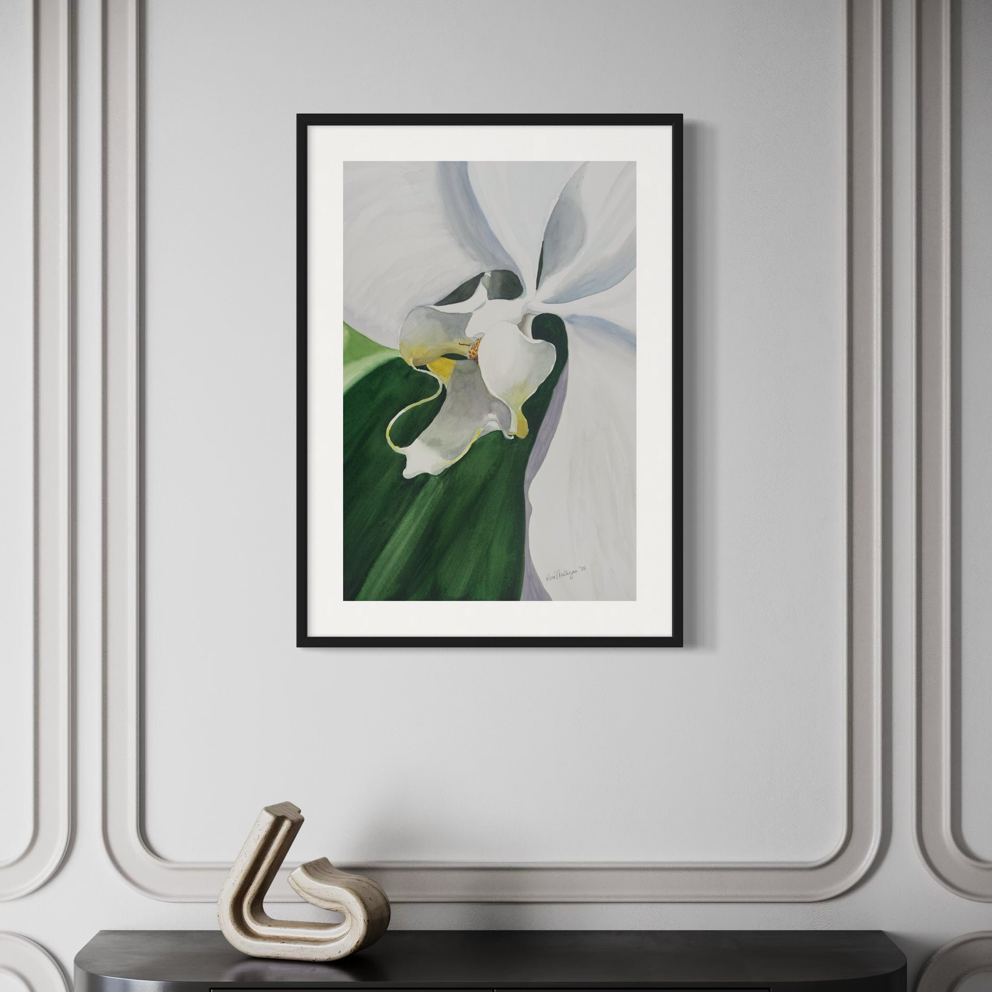 Framed watercolor artwork of a white orchid flower with green leaves on a gray wall.