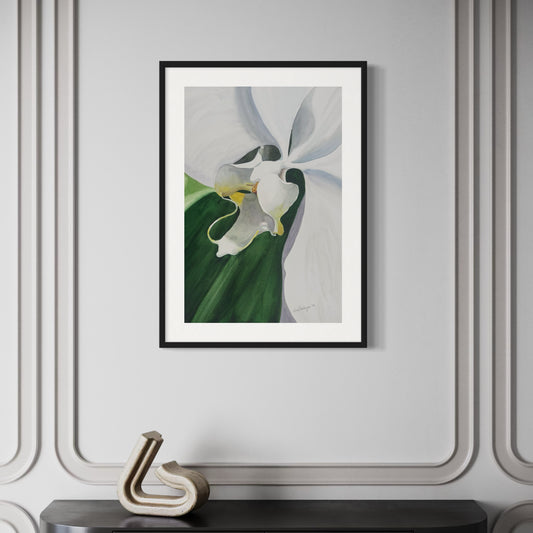 Framed watercolor artwork of a white orchid flower with green leaves on a gray wall.