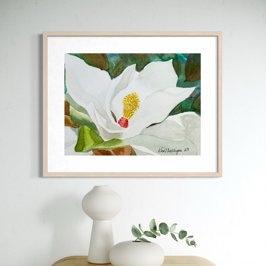 Framed watercolor artwork of a white magnolia flower with green leaves on a light gray wall.
