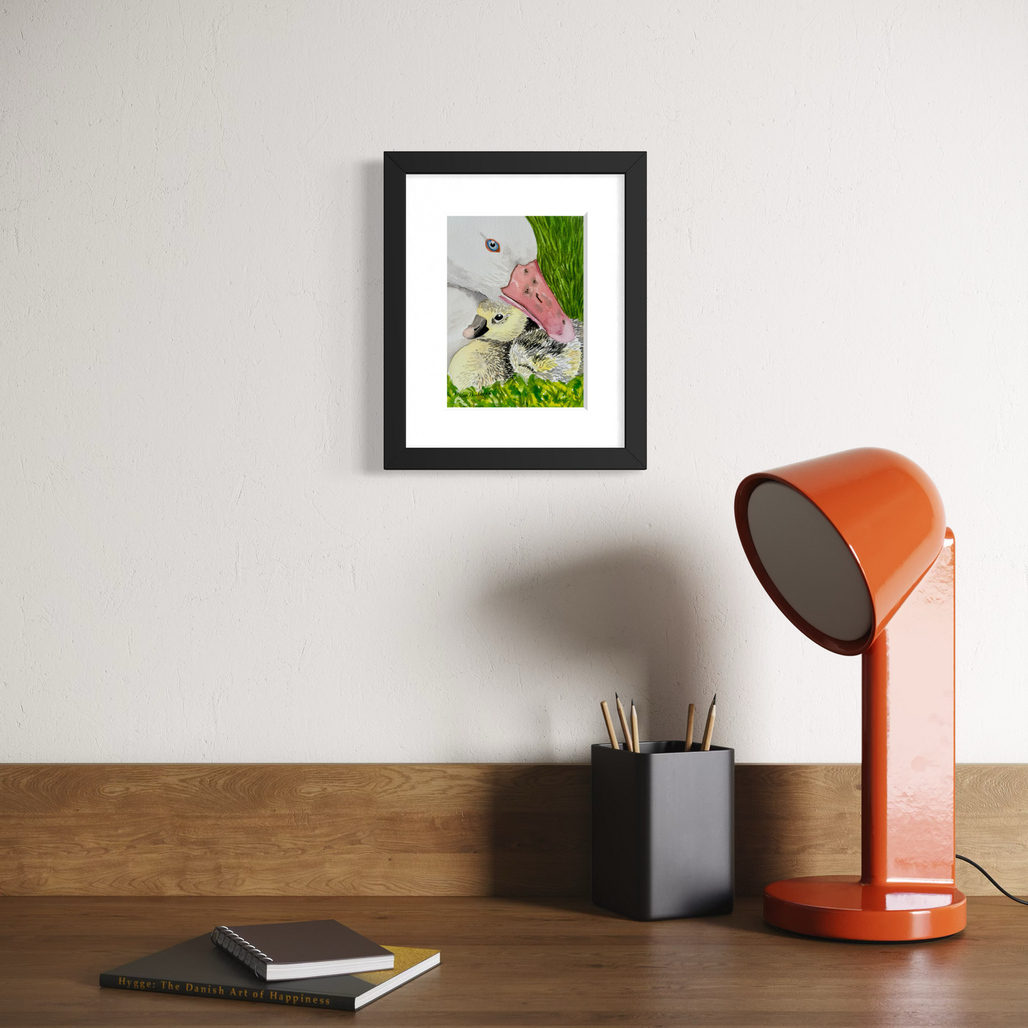 Framed watercolor painting of a white mother duck sheltering her duckling in the grass.