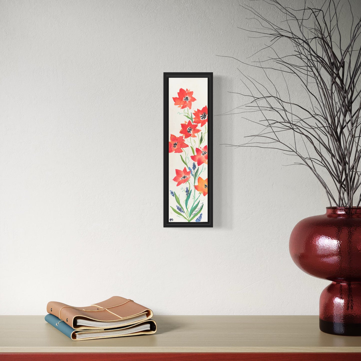 Framed floral artwork with abstract poppies on a wall above a shelf with books and a vase.