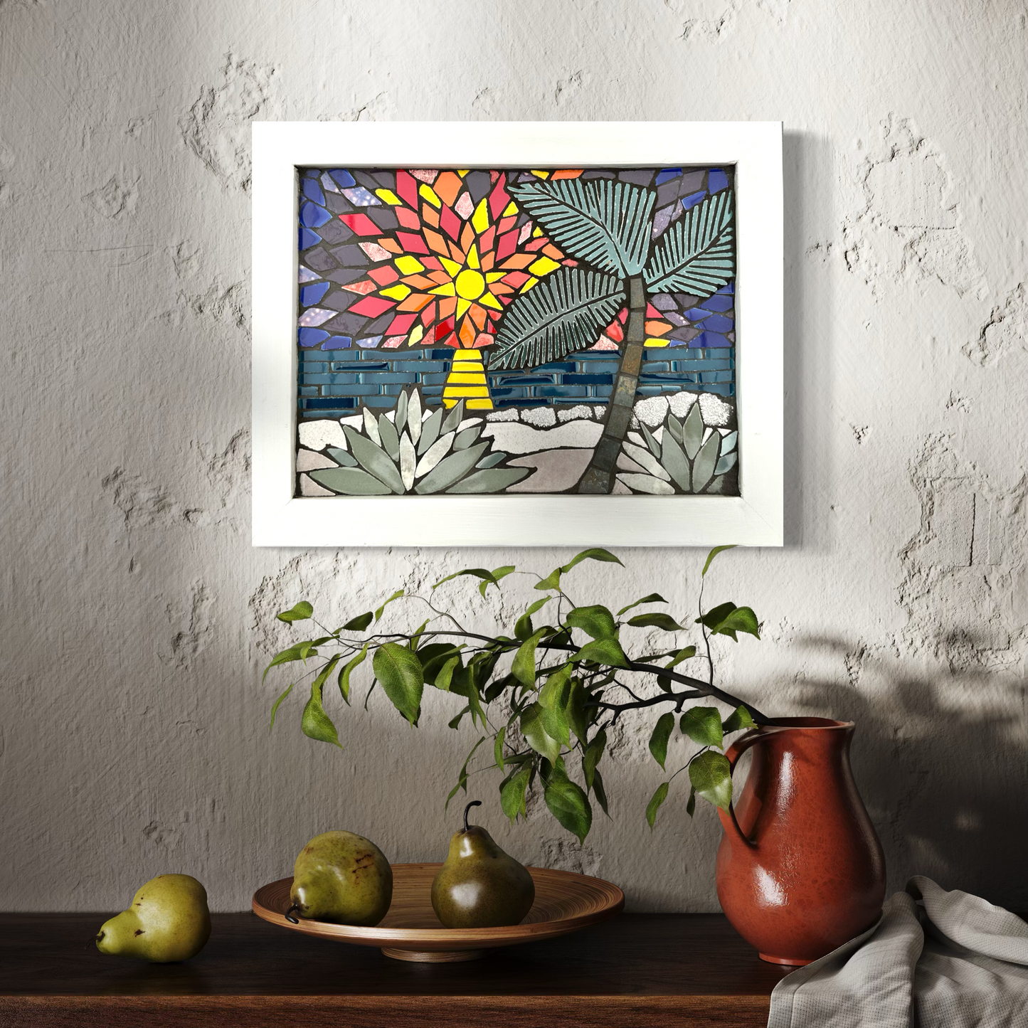 Framed mosaic artwork of a tropical scene with a colorful sunset, palm tree, and plants on a textured wall.