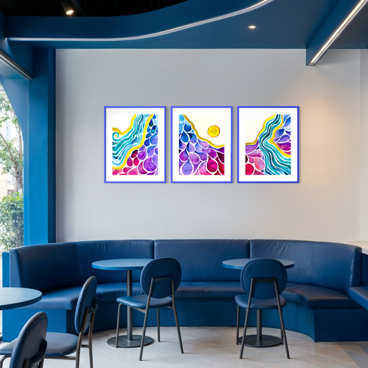 Three framed abstract art prints with colorful wavy patterns are displayed on a white wall above a blue curved seating area in a modern cafe or lounge setting.