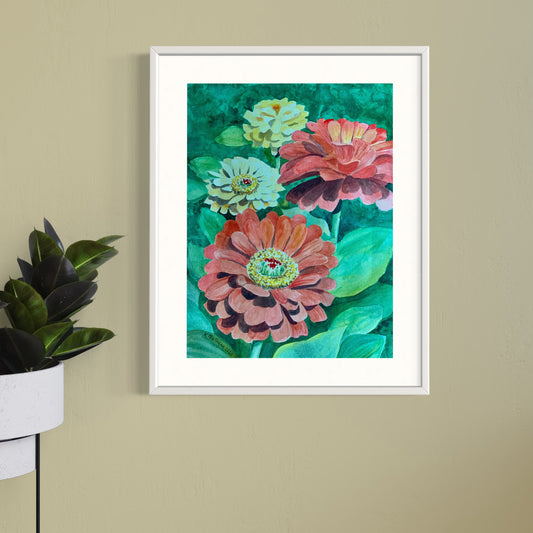 Framed watercolor artwork of yellow and red zinnia flowers on a beige wall with a plant to the left.